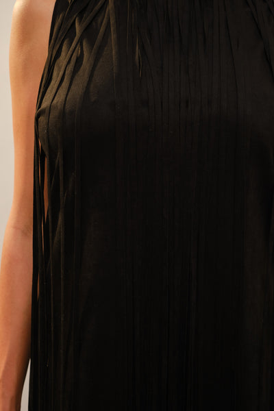Close-up of a black sleeveless dress with a pleated, fringed texture, worn by a model whose arm is visible on the left side.
