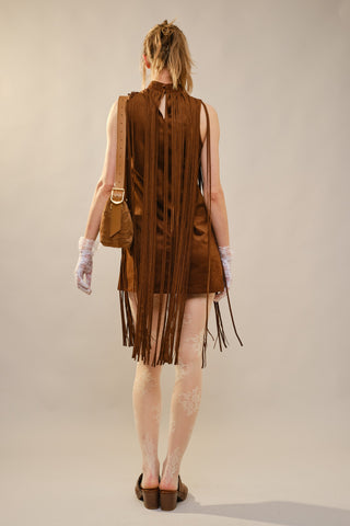 A model shown from behind wearing a brown fringe dress with a high neck, paired with white lace gloves, patterned tights, and brown block-heel mules, against a plain light gray studio background.