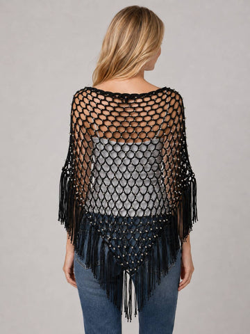 A woman shown from the back wearing a black open-knit fringed poncho over a gray top and blue jeans, against a plain light gray studio background.