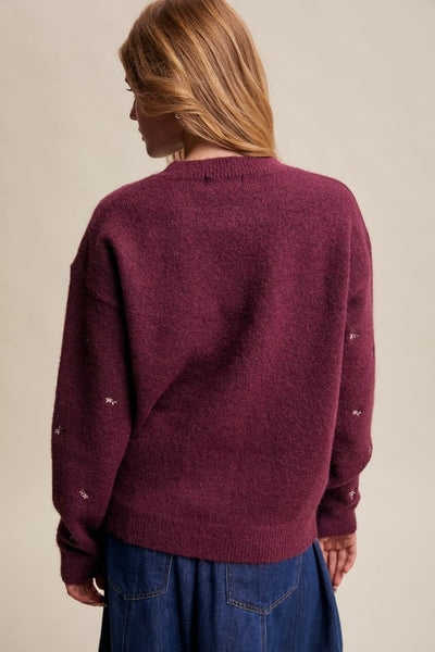 Person wearing a maroon sweater with white buttons on a beige background