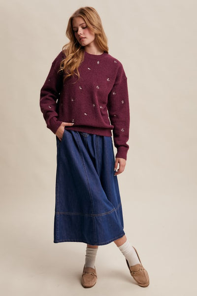 Woman wearing a maroon sweater and blue skirt on a beige background