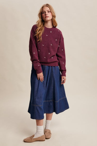 Woman wearing a maroon sweater and blue skirt on a beige background