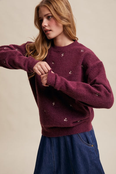 Woman wearing a burgundy sweater with small decorative elements on a beige background