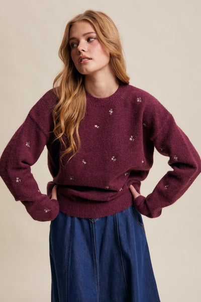 Woman wearing a maroon sweater with small patterns against a beige background