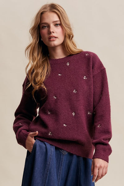 Woman wearing a burgundy sweater with floral embellishments on a beige background