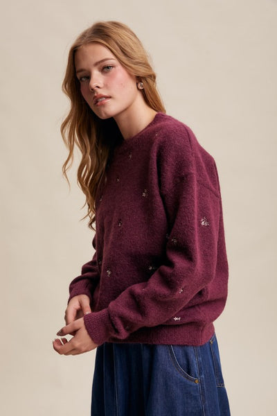 Woman wearing a maroon sweater with a small logo on a beige background