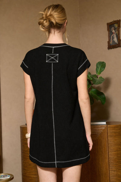 Woman wearing a black dress with a unique back design in a room with a plant and painting.