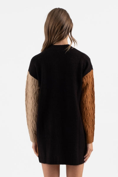 Black sweater with brown sleeves worn by a person on a white background