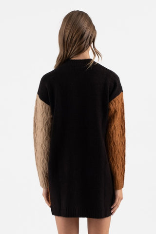 Black sweater with brown sleeves worn by a person on a white background
