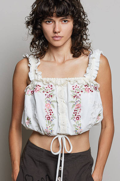 Woman wearing a white floral embroidered top against a plain background