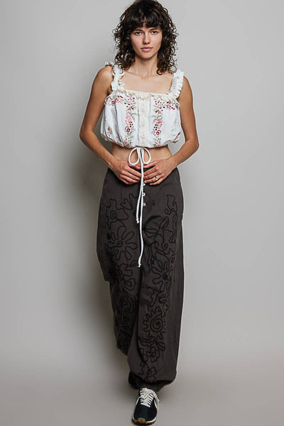 Person wearing a white embroidered top and dark patterned pants on a plain background