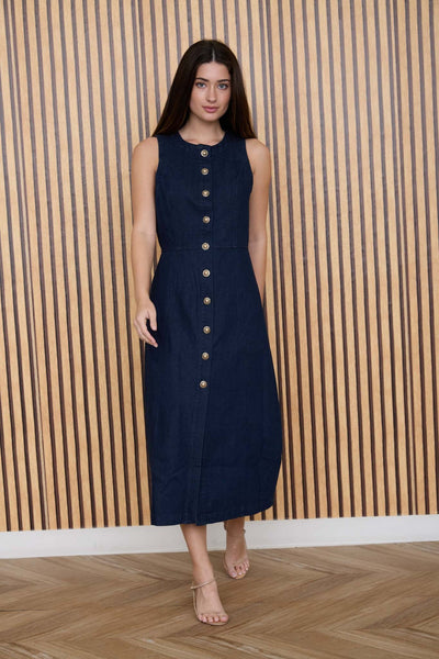 Woman wearing a navy dress with button details against a striped wooden wall.