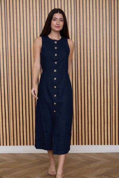 Woman wearing a navy sleeveless dress with buttons against a wooden paneled wall.