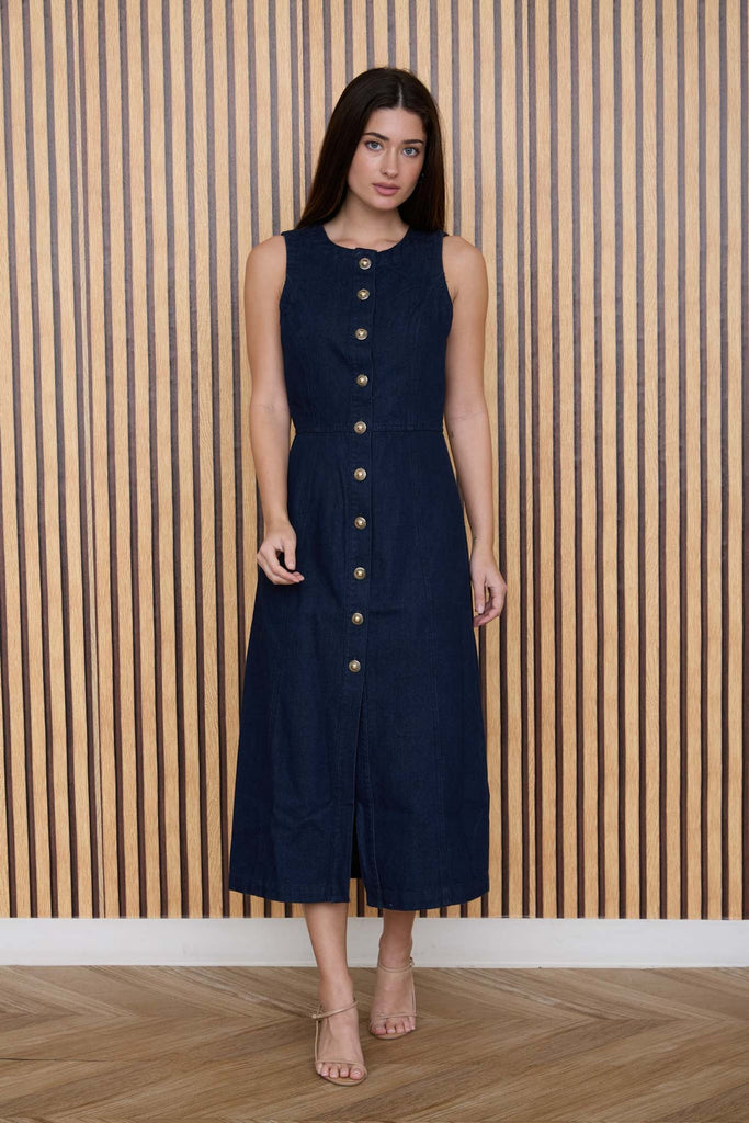 Woman wearing a navy dress with gold buttons against a wooden paneled wall.