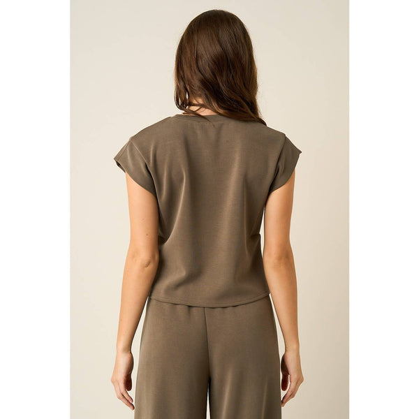 A woman shown from the back wearing a short-sleeve taupe-brown top and matching pants against a plain light beige studio background.