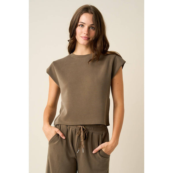 A woman modeling a matching two-piece lounge set in a solid taupe-brown color, featuring a short-sleeve crewneck top and drawstring pants, set against a plain beige studio background.