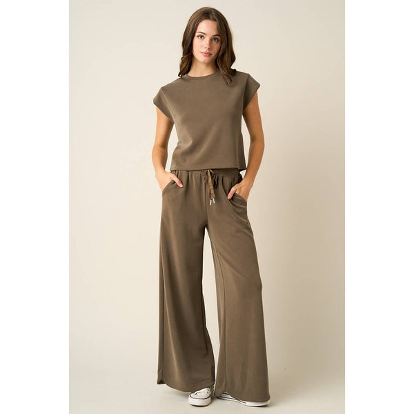 A woman modeling a matching two-piece lounge set in a solid taupe-brown color, featuring a short-sleeve crewneck top and wide-leg drawstring pants, set against a plain beige studio background.