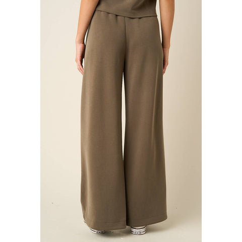 A person wearing high-waisted, wide-leg trousers in a solid taupe-brown color, shown from the waist down against a plain beige studio background.