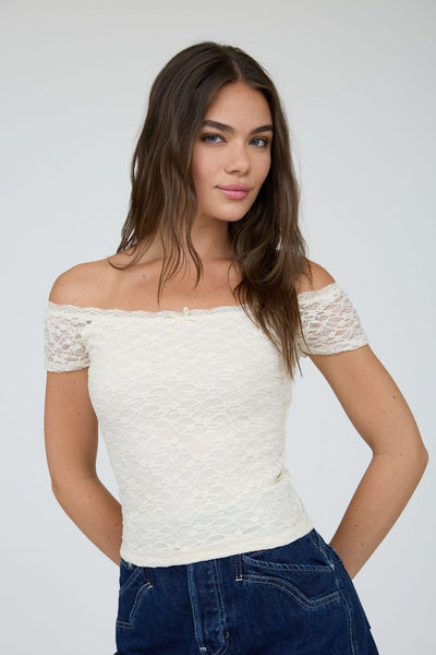 Woman wearing a white off-shoulder top with lace sleeves on a plain background
