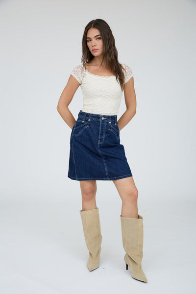 Woman wearing a white top, blue denim skirt, and beige knee-high boots on a white background