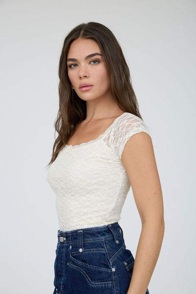 Woman wearing a white textured top and blue jeans against a plain background