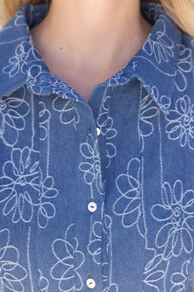 Close-up of a person wearing a blue button-front collared shirt with a white floral line pattern.