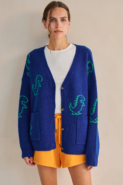 Person wearing a blue cardigan with green dinosaur patterns on a beige background
