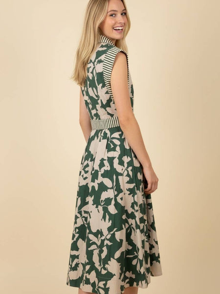 A woman modeling a sleeveless midi dress with a green and beige floral pattern, striped bodice details, and a matching striped belt, set against a solid beige background.