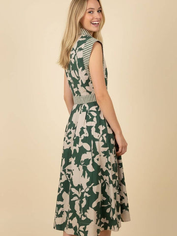 A woman modeling a sleeveless midi dress with a green and beige floral pattern, striped bodice details, and a matching striped belt, set against a solid beige background.