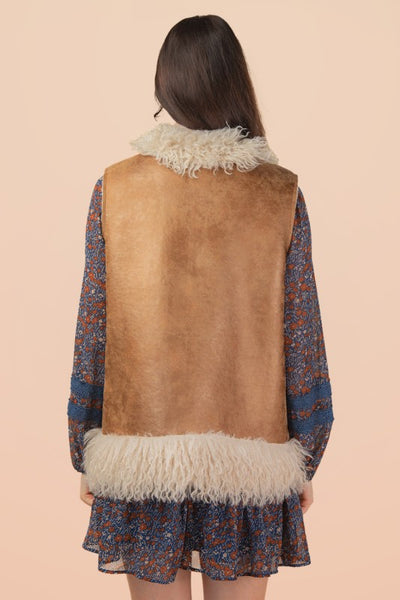 Person wearing a patterned dress with a brown vest and white fur trim on a beige background