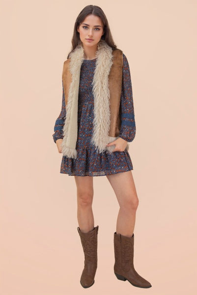 Woman wearing a patterned dress with a fur vest and boots on a beige background