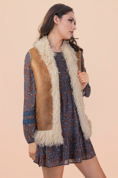 Woman wearing a patterned dress with a brown and white vest against a beige background