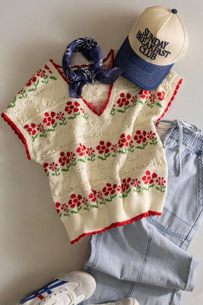Floral-patterned sleeveless top with denim shorts, sneakers, and a cap on a neutral background