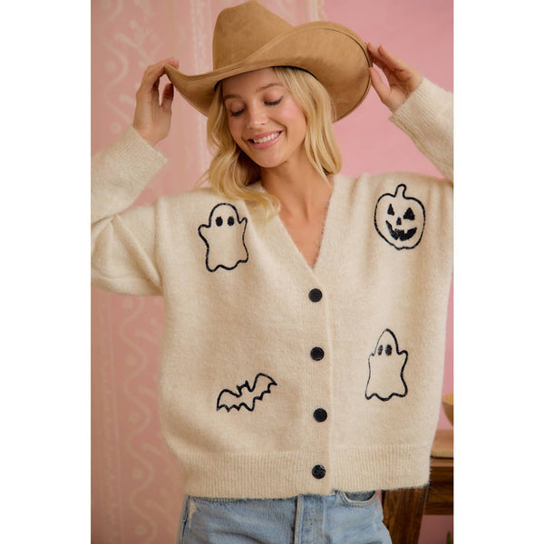 Woman wearing a beige cardigan with Halloween graphics against a pink background
