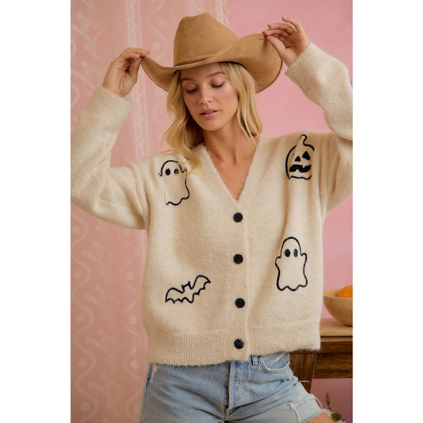 Woman wearing a beige cardigan with Halloween-themed graphics against a pink background
