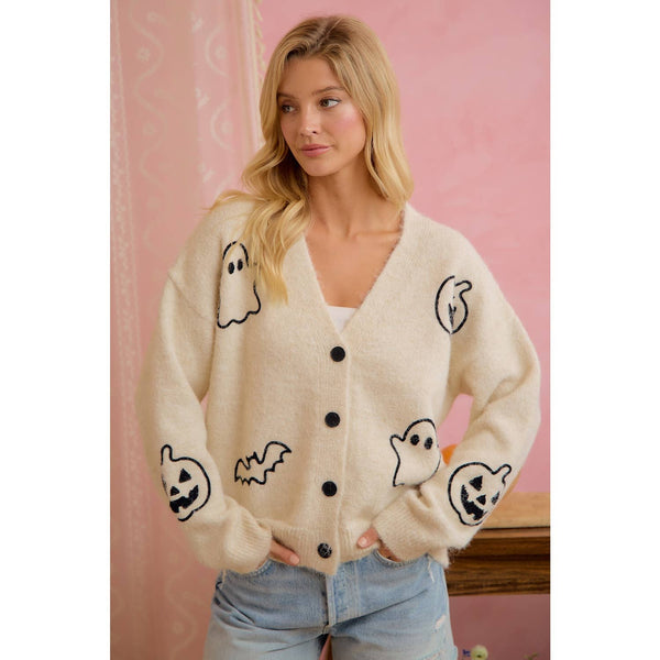 Woman wearing a cream cardigan with Halloween-themed graphics against a pink background