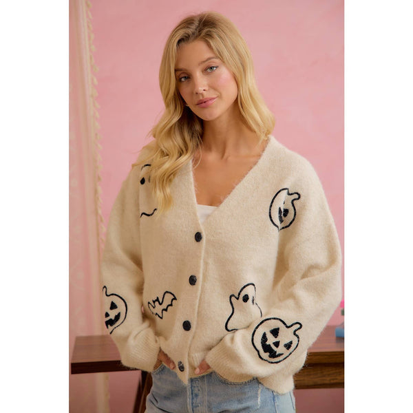 Woman wearing a cream cardigan with black ghost and pumpkin designs against a pink background