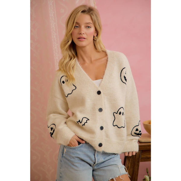 Woman wearing a cream cardigan with black ghost designs against a pink background