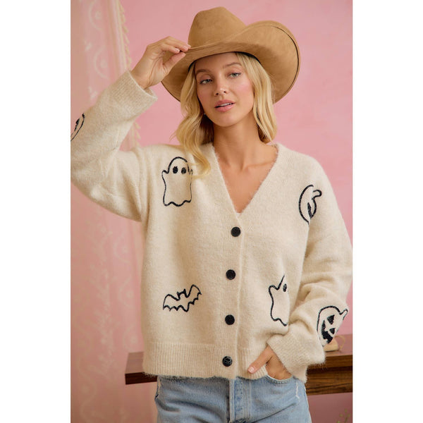 Woman wearing a cream cardigan with black graphics and a beige hat against a pink background