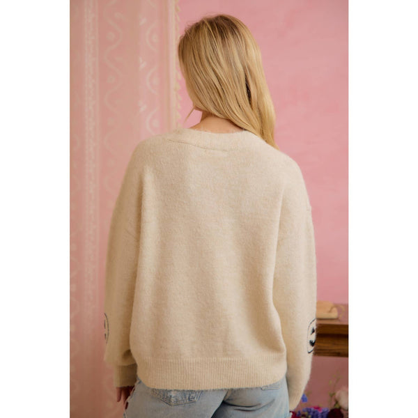 Person wearing a beige sweater with a pink wall in the background