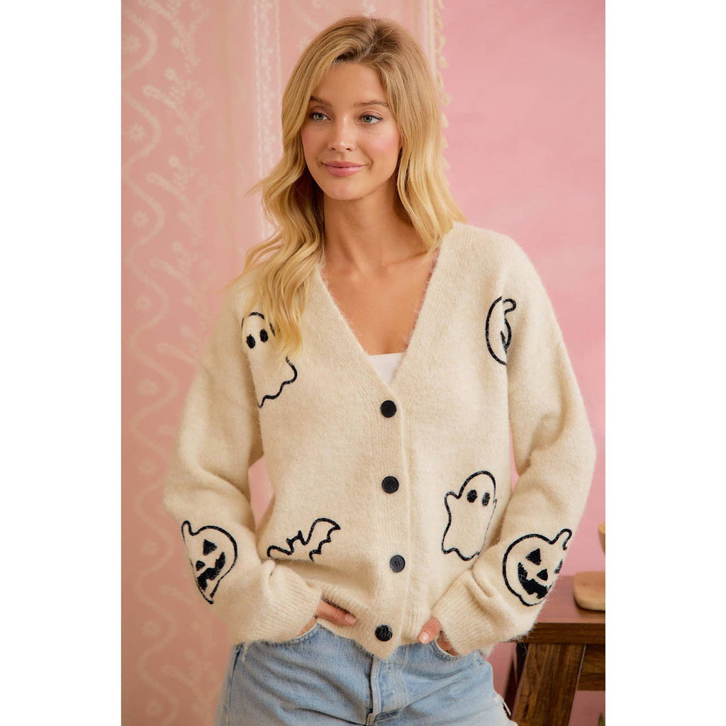 Woman wearing a cream cardigan with ghost designs against a pink background