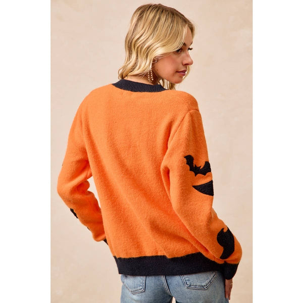 A woman wearing a fuzzy orange sweater with black trim and a black bat motif on the sleeve, shown from the back against a plain beige background.