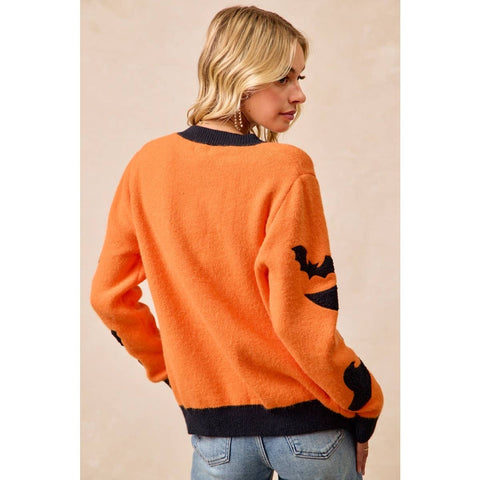A woman wearing a fuzzy orange sweater with black trim and a black bat motif on the sleeve, shown from the back against a plain beige background.