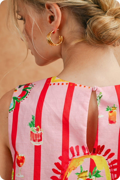 Close-up of a person wearing a colorful sleeveless top with fruit and drink graphics, gold hoop earrings.