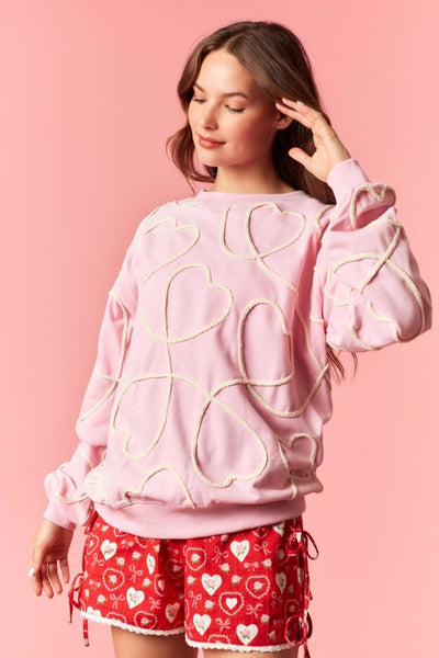 Woman wearing a pink sweatshirt with gold heart designs and red shorts with heart patterns on a pink background
