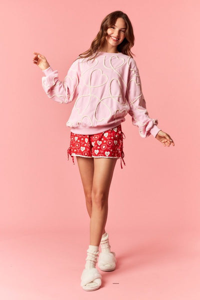 Woman wearing a pink sweatshirt and red shorts with white hearts on a pink background