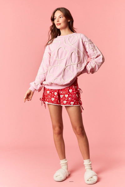 Woman wearing a pink sweatshirt and red shorts with white hearts on a pink background