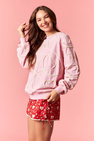 Woman wearing a pink sweatshirt with heart designs and red shorts with white patterns on a pink background