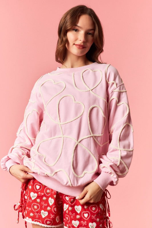 Woman wearing a pink sweatshirt with heart designs on a pink background