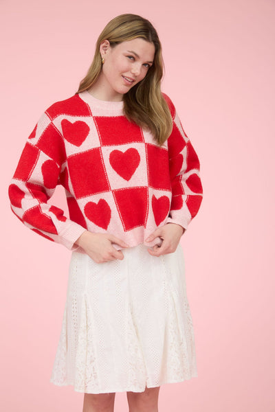 Woman wearing a red and white checkered sweater with heart patterns on a pink background
